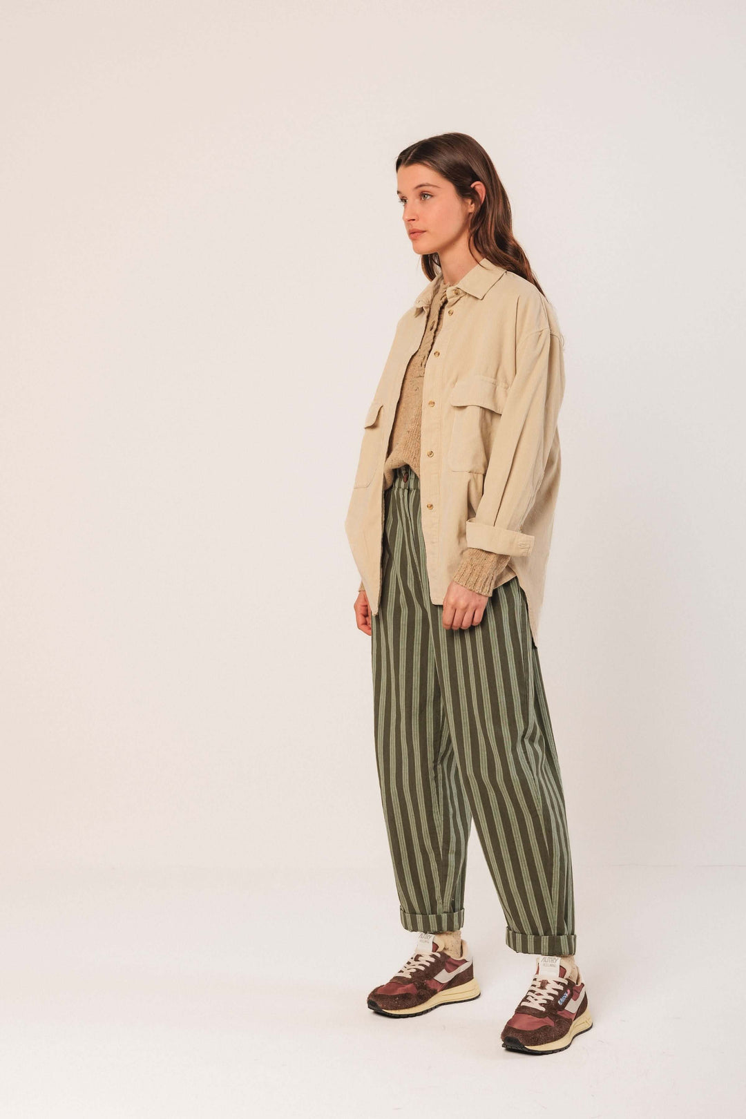 Modèle portant une veste en velours côtelé beige avec pantalon à rayures et baskets, illustrant le style décontracté et tendance.
