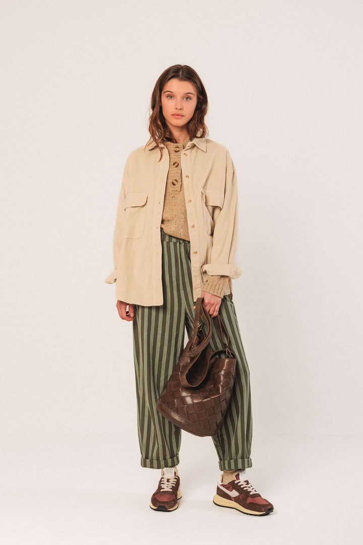 Femme portant une veste en velours côtelé beige avec un pantalon à rayures et un sac marron, style casual chic.
