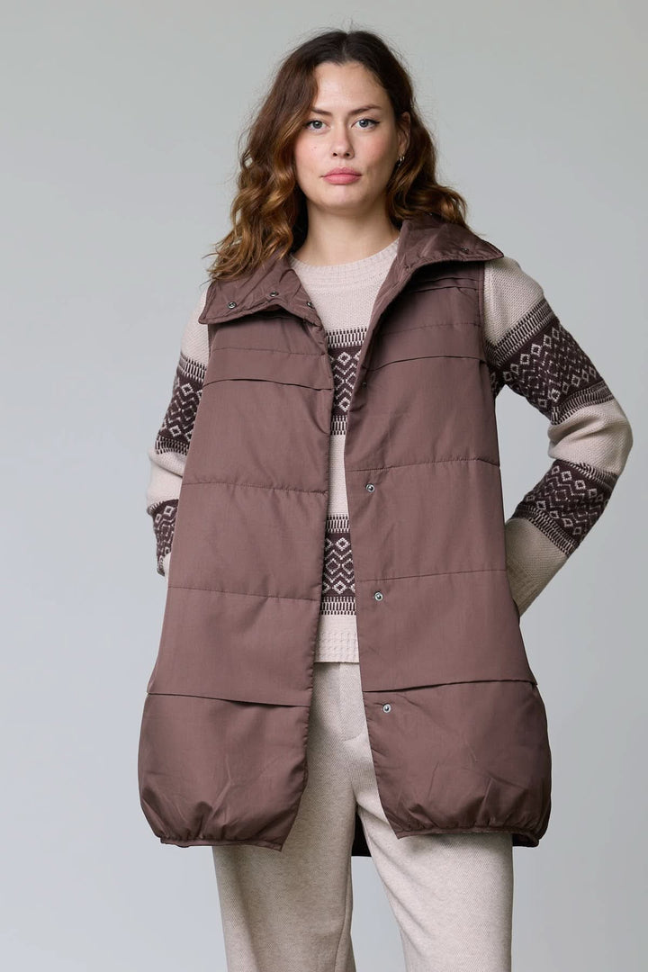 Veste sans manches matelassée longue marron avec col montant et fermeture à glissière, portée par une femme pour un look élégant