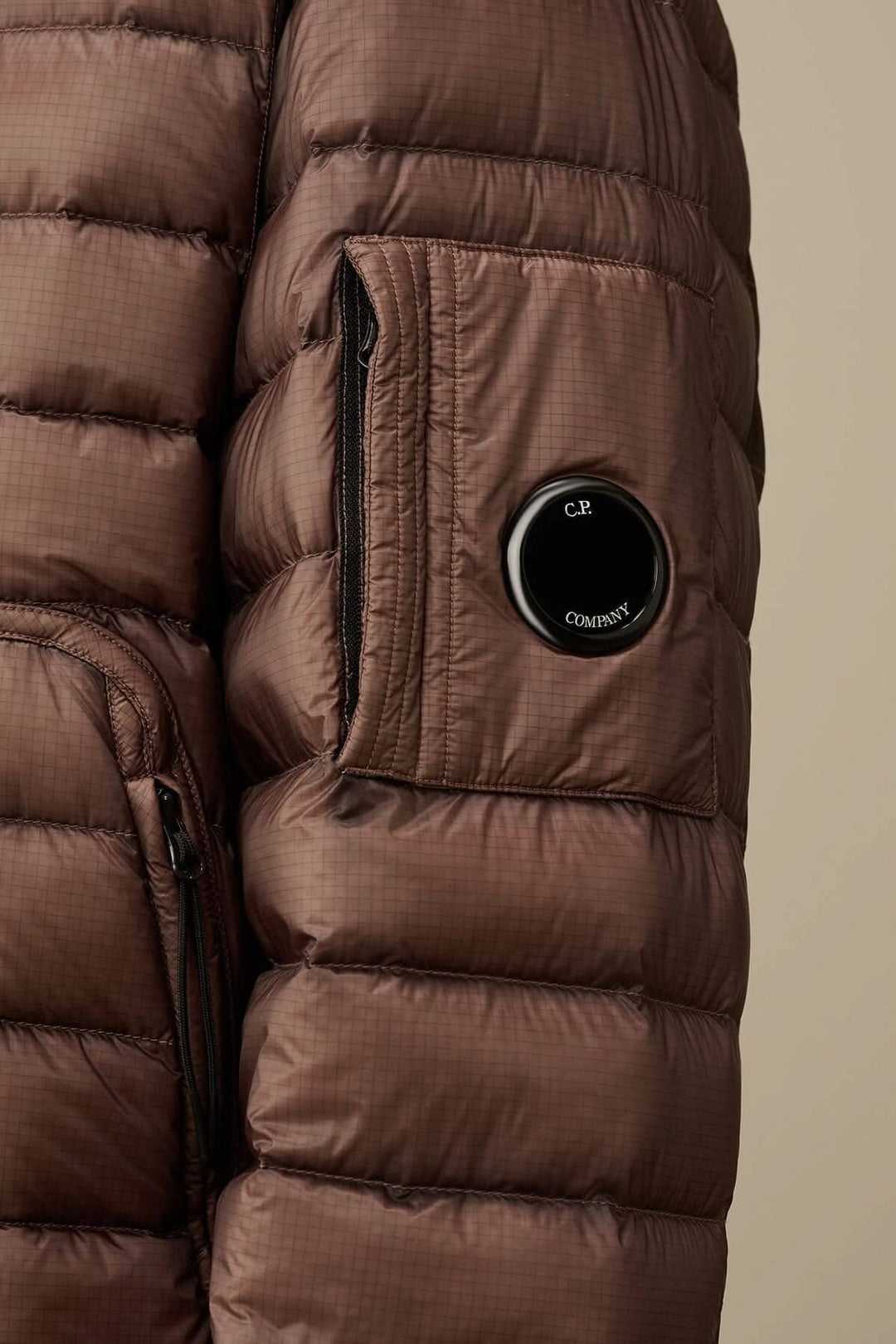 Zoom sur une doudoune brune avec poche zippée et détail de lentille, en tissu léger D.D. Shell.