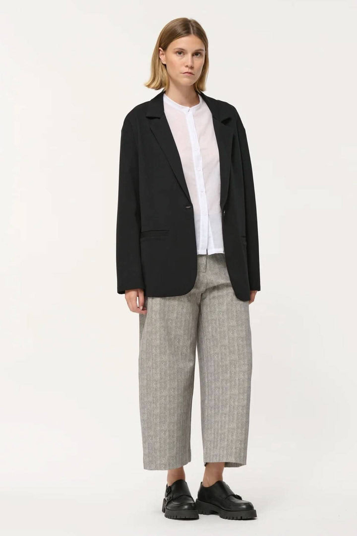 Veston Cayden noir à coupe droite, manches longues, porté avec chemise blanche et pantalon ample.