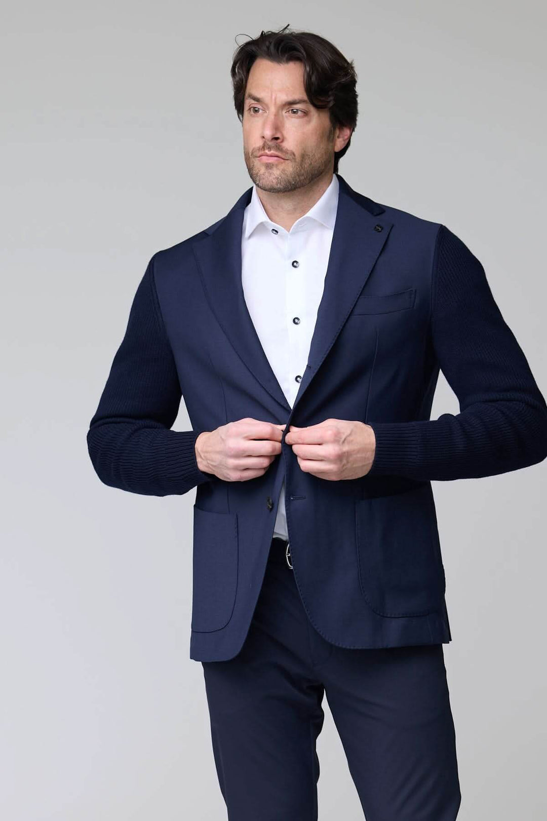 Homme portant un veston hybride tricot et tissu bleu marine, élégant et moderne, avec un col à revers classique et manches en maille.