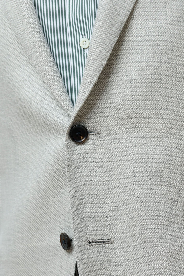 Détail du veston texturé en laine, soie et lin avec boutonnière et motifs à rayures en dessous.