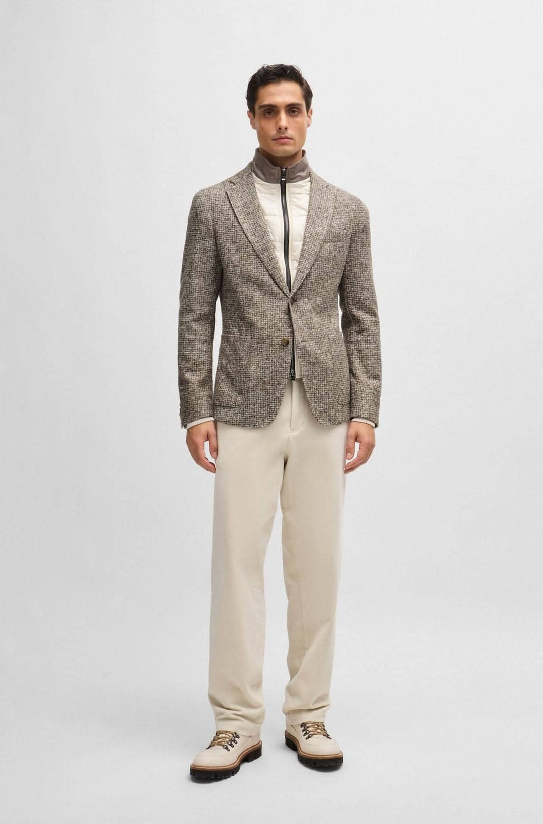 Homme portant une veste texturée avec encolure amovible, pantalon beige, style moderne et raffiné.