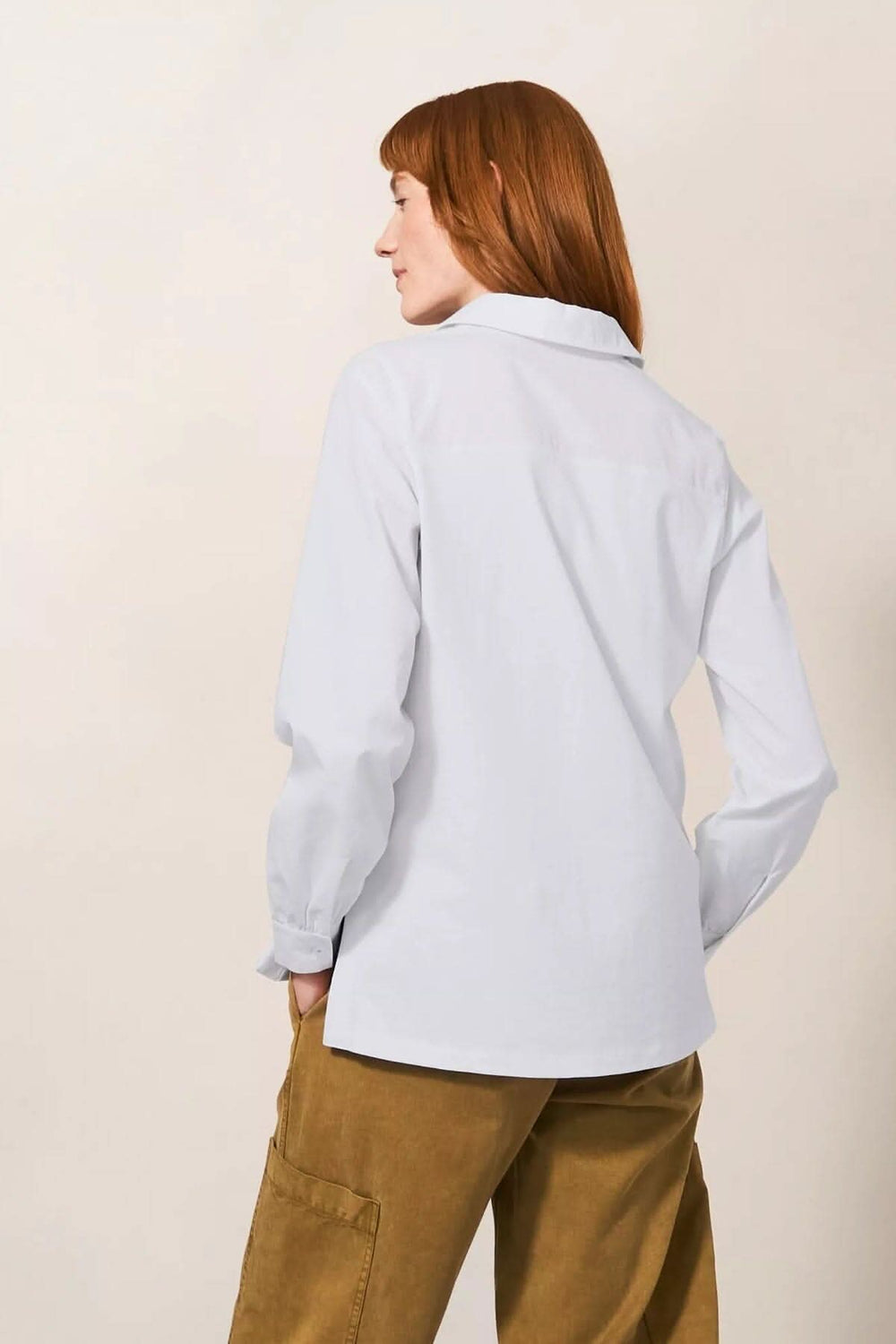 Vue arrière d'une chemise à manches longues blanche avec col en V, portée par une femme.