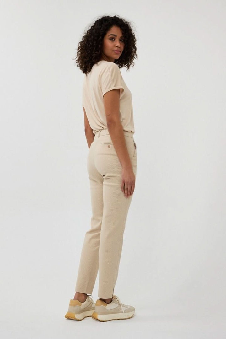 Femme portant un pantalon droit en jacquard texturé, vue de derrière, avec t-shirt beige et sneakers tendance.