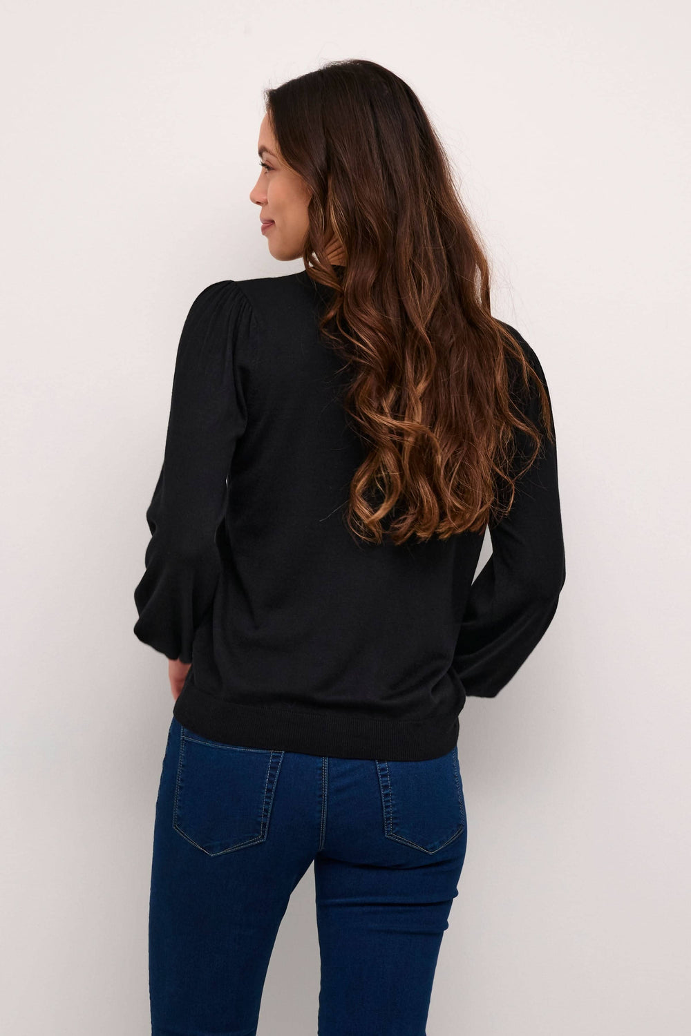 Femme portant le cardigan Lizza noir à manches ballons, vu de dos, avec un style classique et polyvalent.