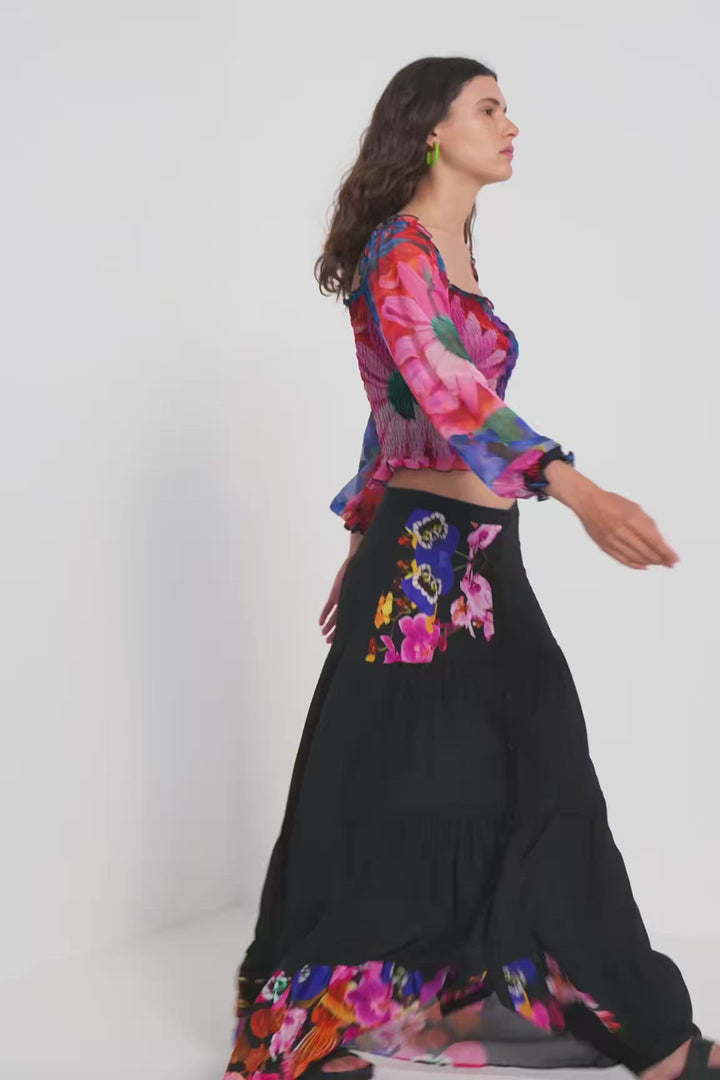 Femme marchant en jupe longue bohème noire avec imprimé florale et blouse colorée, style chic et éco-durable.
