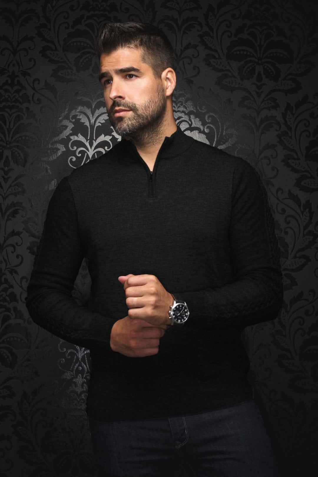 Homme portant un chandail col zip Mesta noir en laine mérinos, devant un fond élégant et sombre.