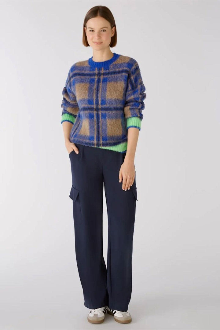 Femme portant un pull à carreaux aux couleurs vives et pantalon cargo large, pose décontractée.