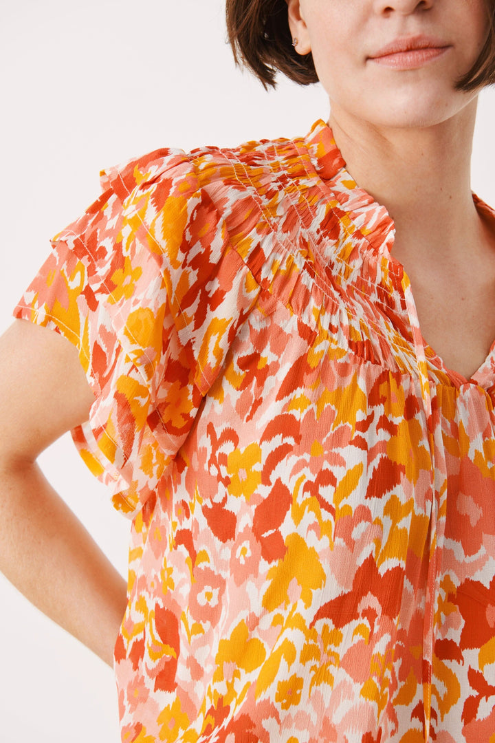 Blouse fleurie Sinna avec manches courtes volantées, imprimé coloré et col montant, pour un style élégant.