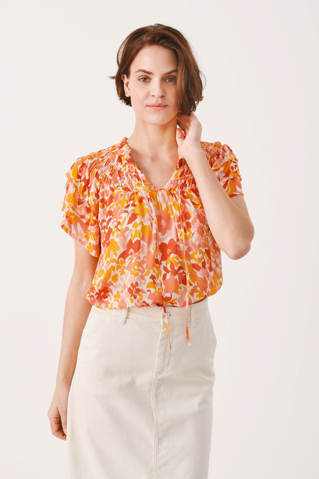 Femme portant une blouse fleurie Sinna, manches courtes, col montant, imprimé coloré sur fond clair.