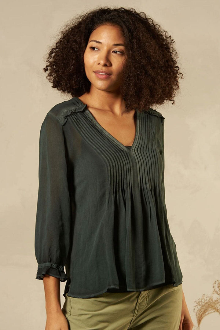 Blouse décontractée col en V, avec détails de couture, style moderne, portée par un modèle avec cheveux bouclés.