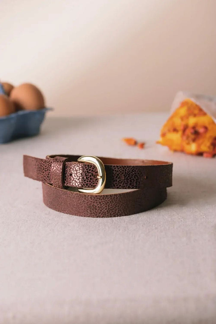 Ceinture en cuir brun avec boucle métallique, sur une table avec des œufs et un muffin.