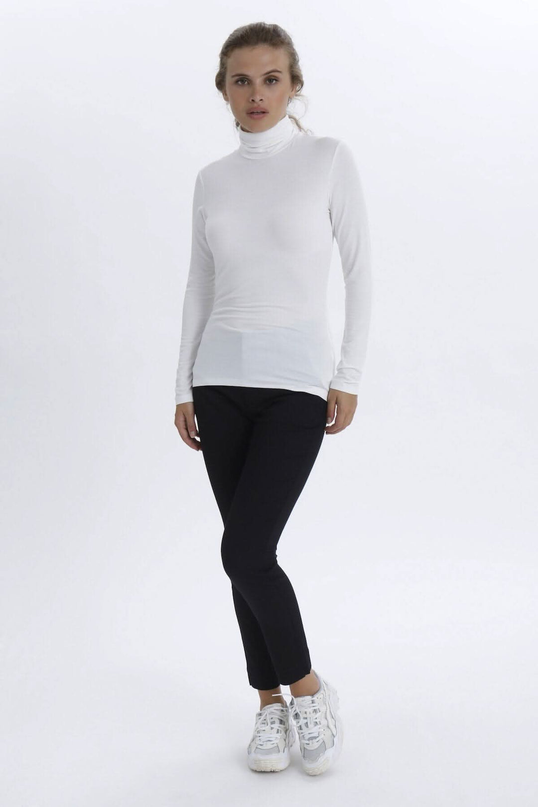 Chandail à col roulé blanc, manches longues, coupe ajustée, porté avec un pantalon noir et des baskets blanches.