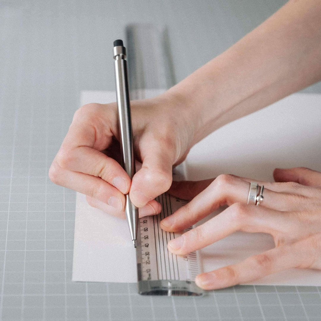 Main image of a person using a crayon on paper with a ruler to create precise drawings.