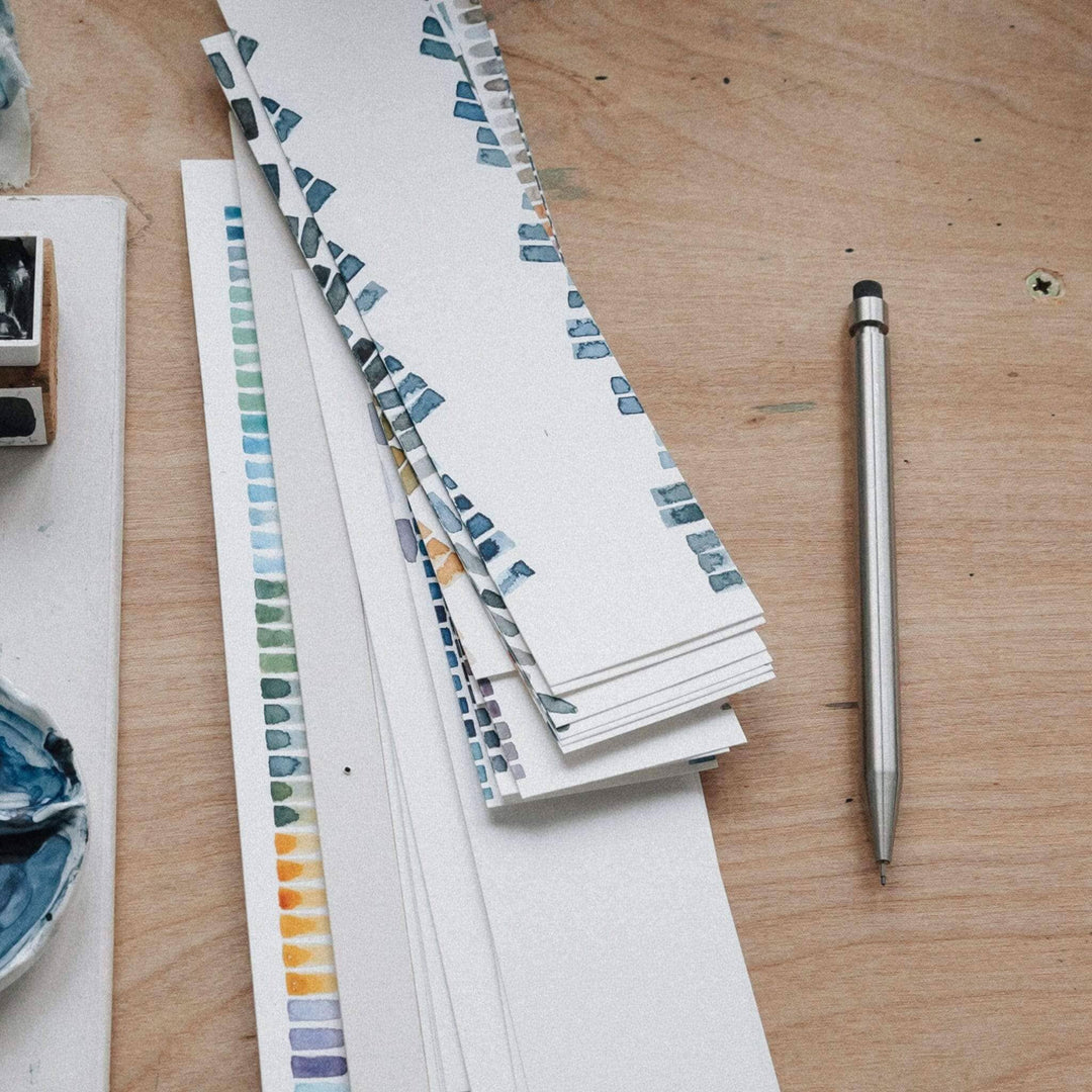 Dessin artistique avec des échantillons de couleurs sur papier et un crayon métallique sur une table en bois.