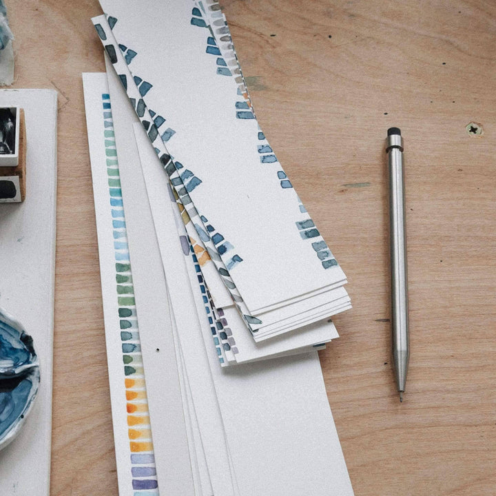 Échantillons de couleurs et croquis sur une table en bois, avec un crayon en métal à côté.