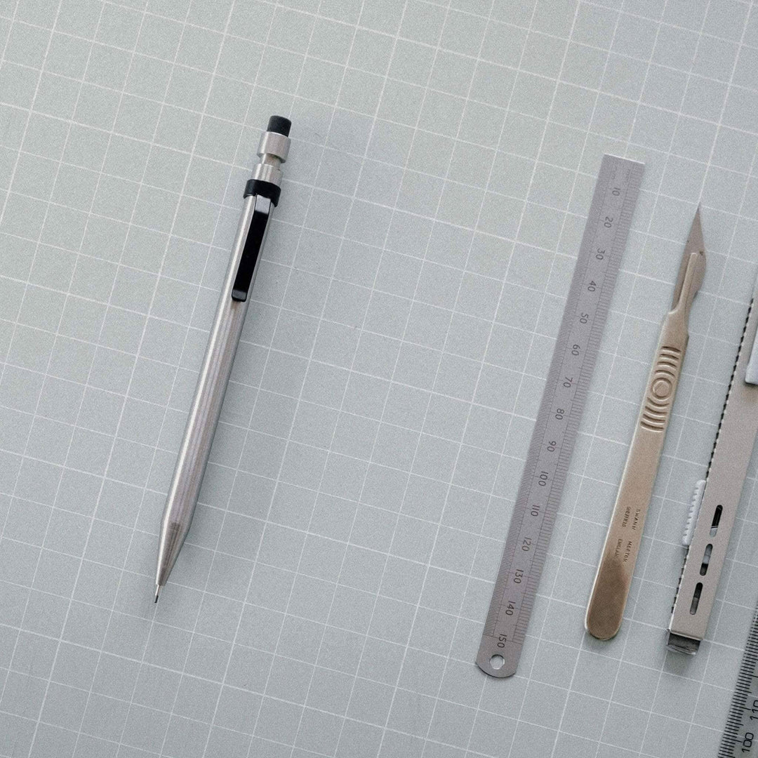 Crayon Modern Fuel en métal solide, avec règle, scalpels et autres outils de précision sur fond gris.