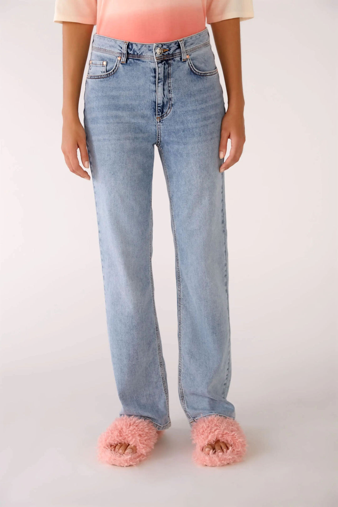 Jean à taille haute avec jambe droite, style classique à cinq poches et coutures contrastées, porté avec des pantoufles roses.