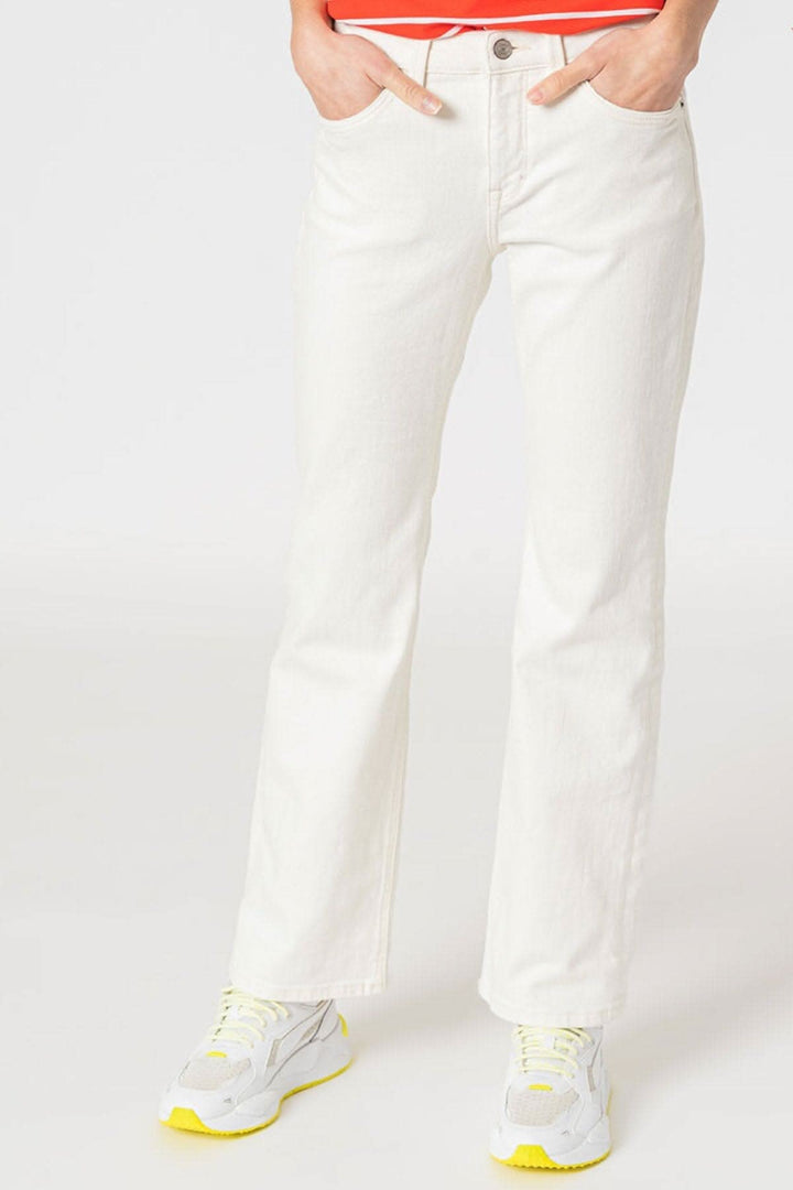 Jean bootcut blanc, cinq poches, coupe ajustée, porté avec des sneakers jaunes.