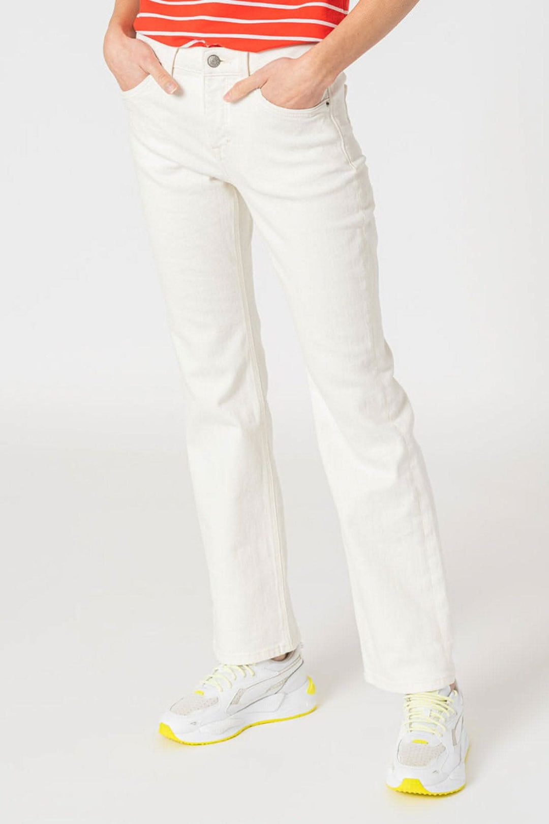 Jean bootcut blanc en coton, ajusté et élégant, porté avec des sneakers et un haut rayé.