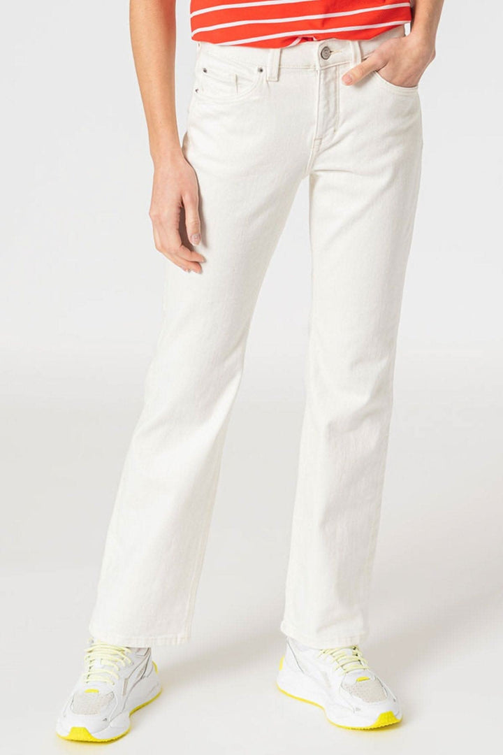 Jean bootcut blanc en coton, ajusté avec cinq poches, porté avec des baskets blanches et un top rayé.
