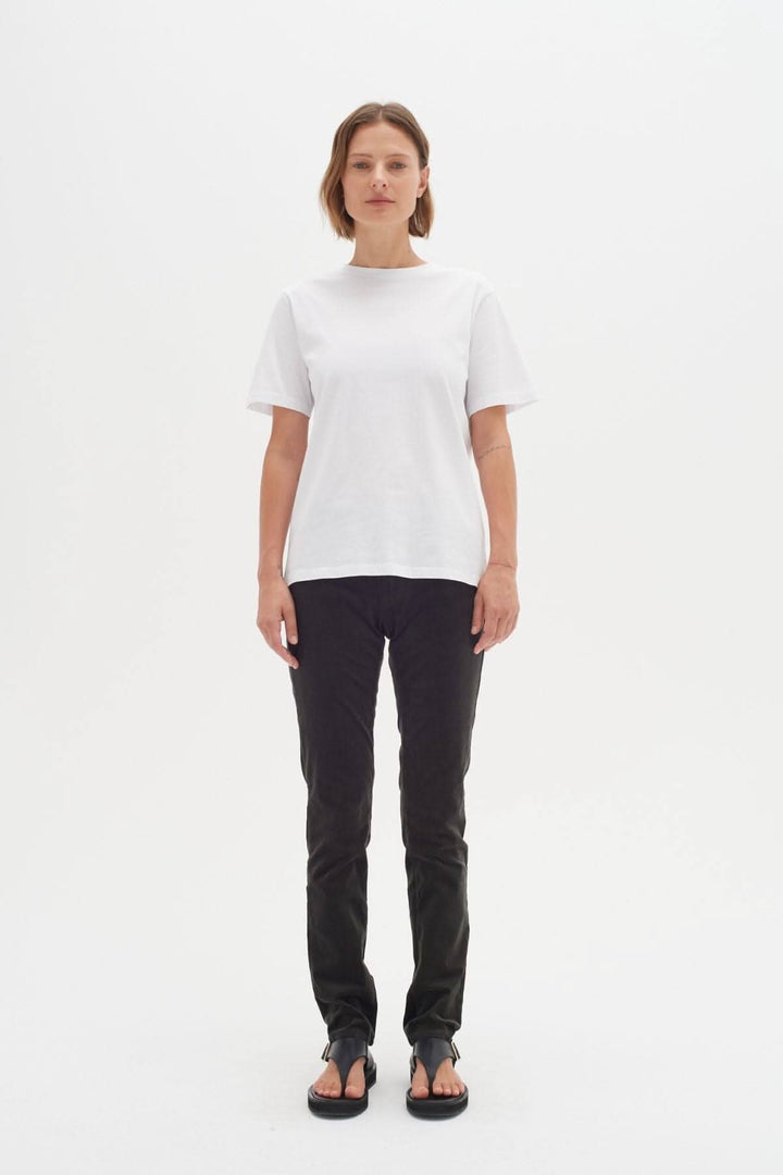Femme portant un t-shirt blanc et un jean ajusté, posant sur fond blanc.