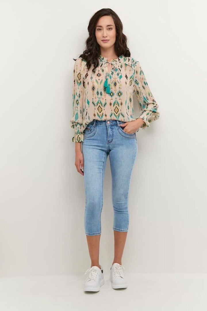 Femme portant un jean trois-quarts bleu clair avec un haut imprimé et des baskets blanches.