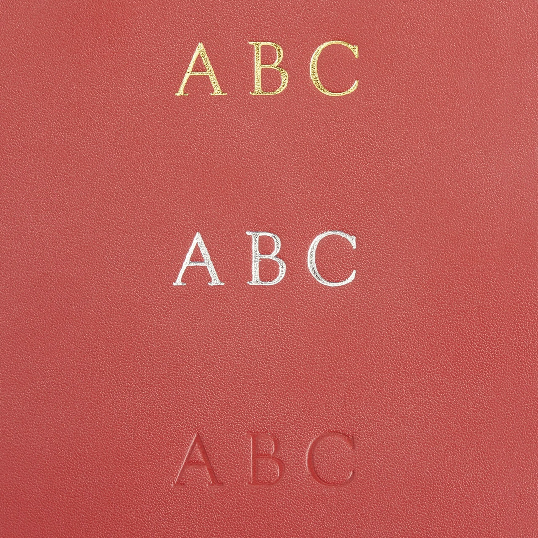 Close-up of a leather surface featuring three monogram styles: gold, silver, and embossed letters &