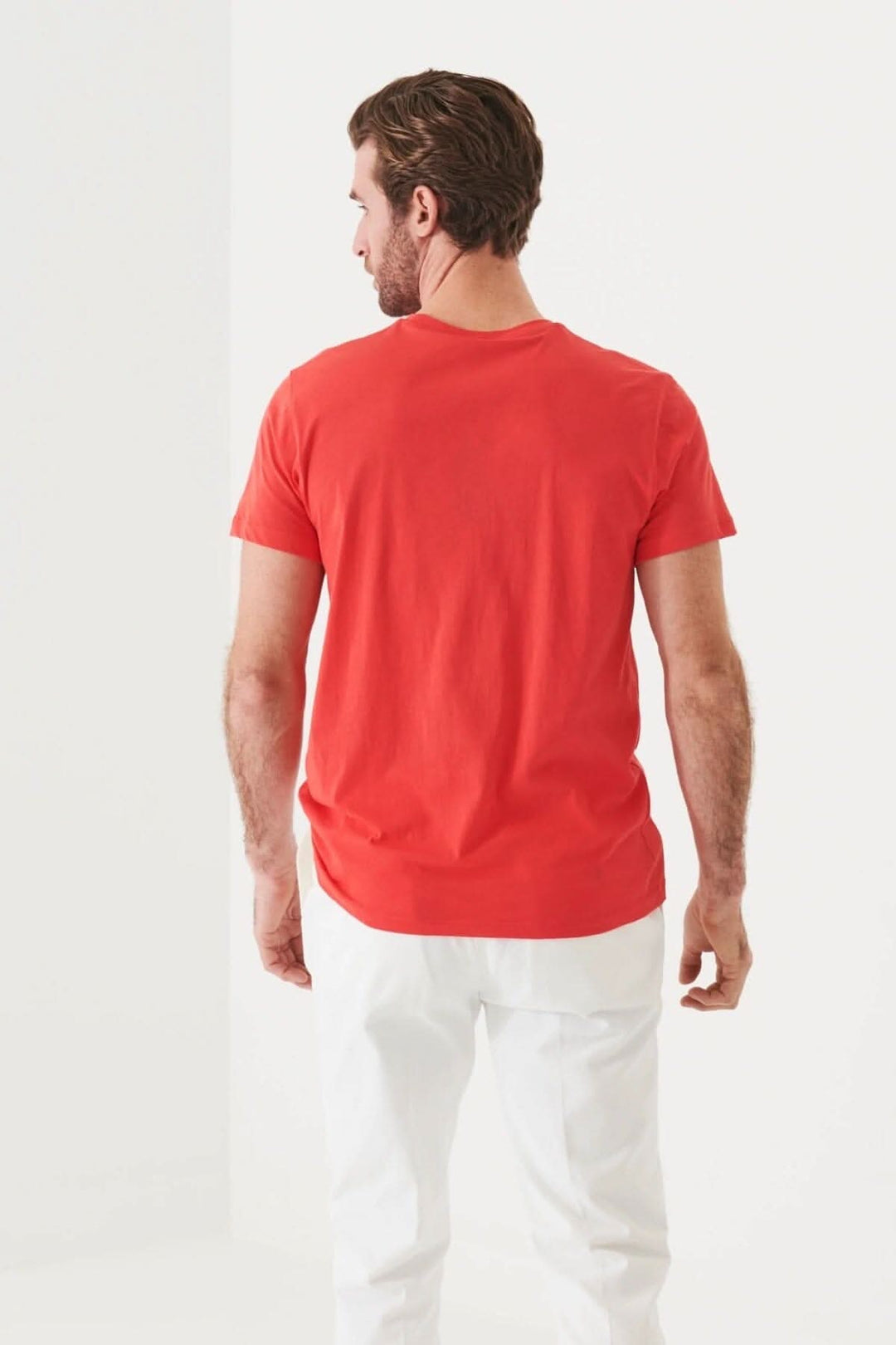 Homme portant un t-shirt léger en coton pima rouge, vu de dos, avec pantalon blanc, dans un environnement lumineux.
