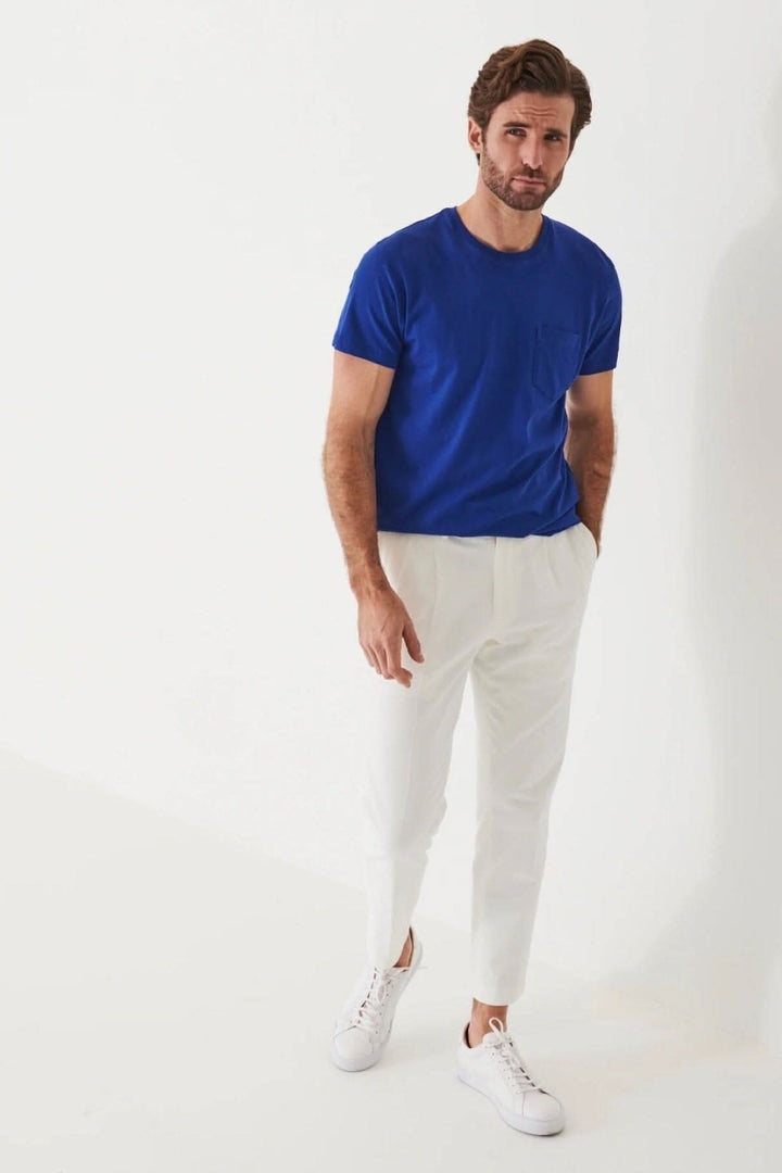 Homme portant un t-shirt léger en coton pima bleu avec une poche, associé à un pantalon blanc.