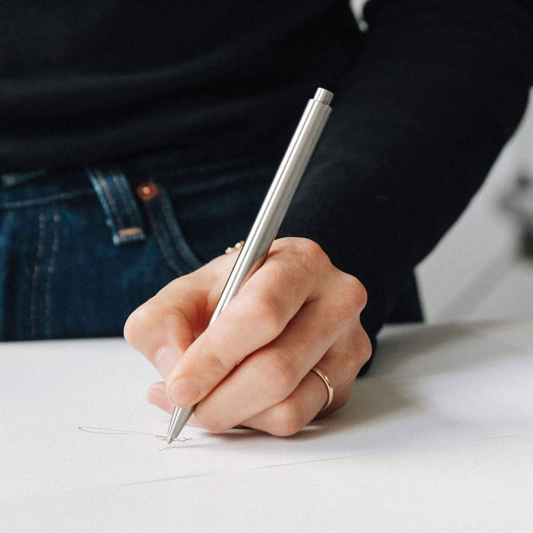 Main user holding Stylo Modern Fuel silver pen, sketching on white paper, stylish design and ergonomic grip.