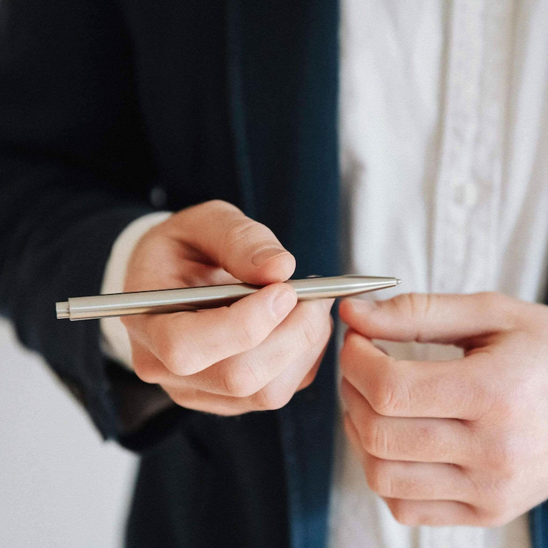 Un homme en costume tient un stylo moderne en métal, parfait pour un usage professionnel et élégant.
