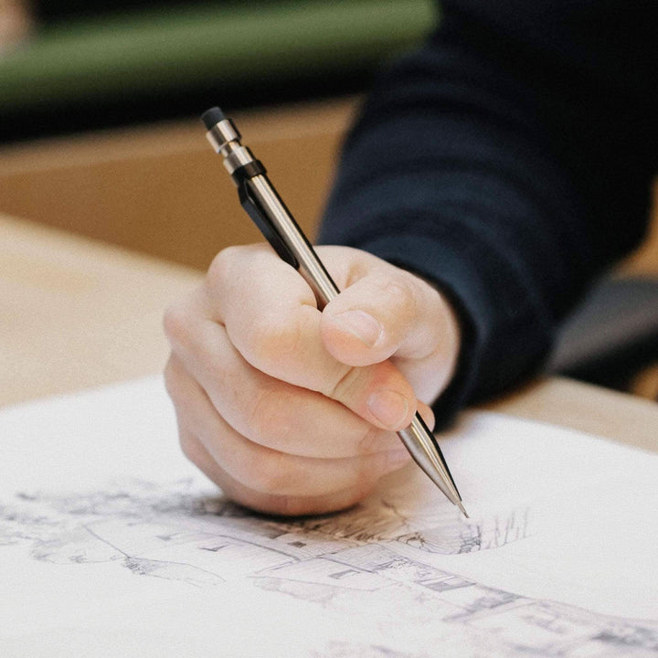 Main image of a hand holding a Crayon Modern Fuel, sketching on paper, showcasing its unique design.