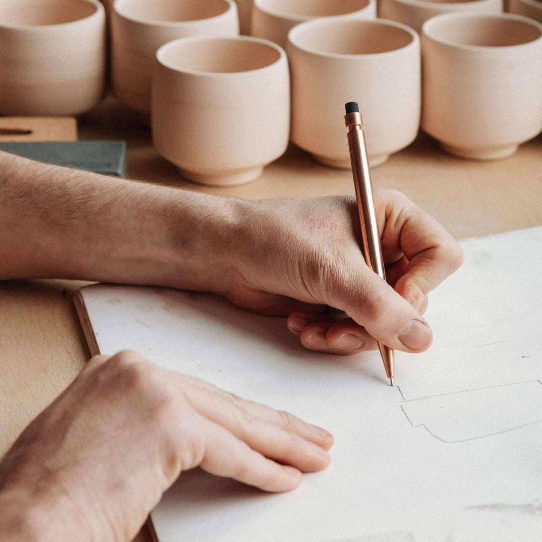 Un artiste dessine avec un crayon Modern Fuel, entouré de tasses en céramique sans ébauche.