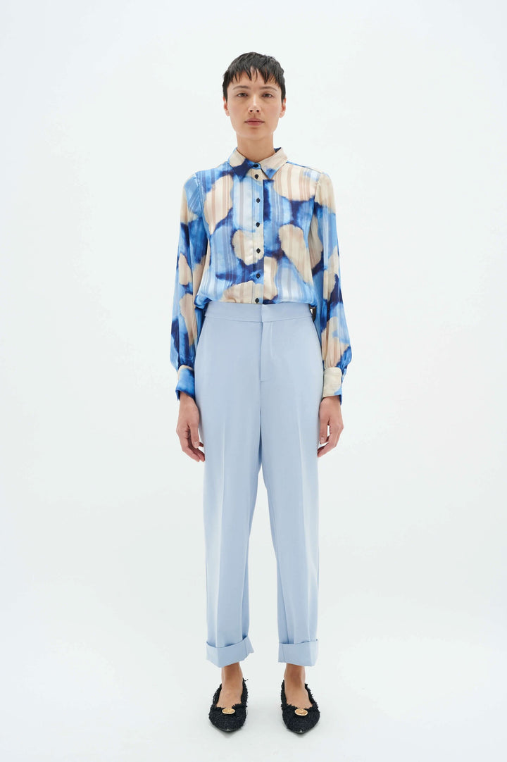 Femme portant une chemise à motifs colorés et un pantalon bleu clair à revers, sur fond blanc.