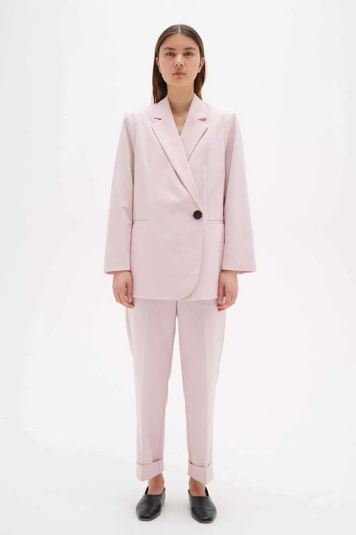 Femme portant un tailleur rose clair avec un pantalon à revers et une veste à bouton pour un look élégant.