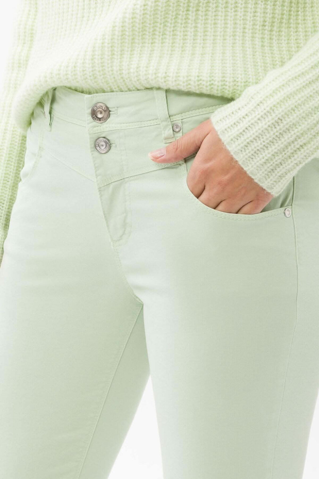 Pantalon skinny vert pastel en détail avec chandail en tricot, mettant en valeur les poches et les boutons.