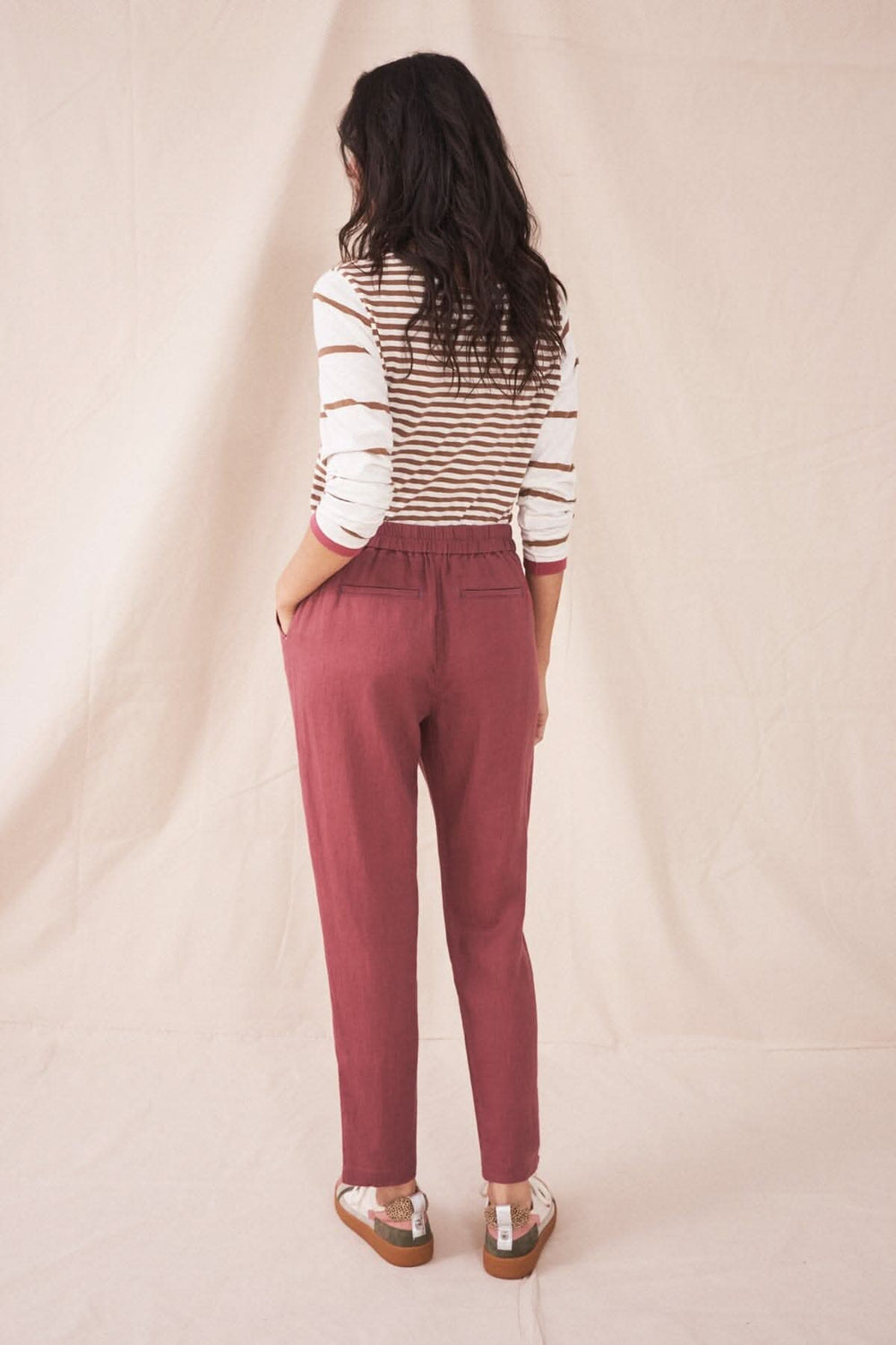 Femme portant le pantalon Maddie en lin rose, vu de dos, avec un top rayé sur fond neutre.