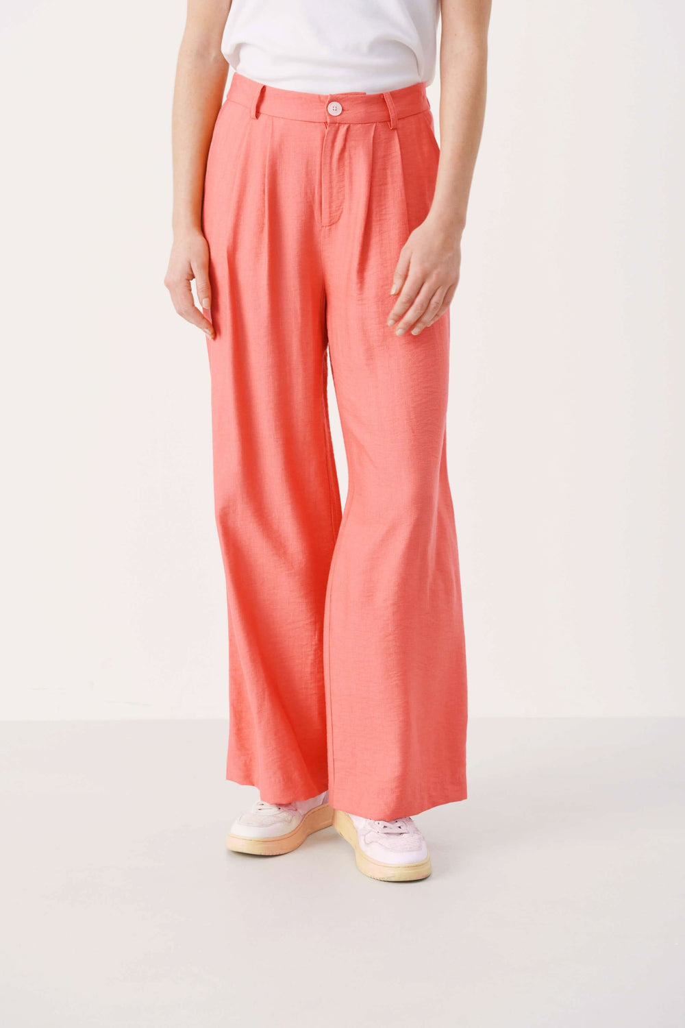 Pantalon habillé Sibille à jambe large en tissu fluide, couleur corail, avec ceinture et fermeture à bouton.