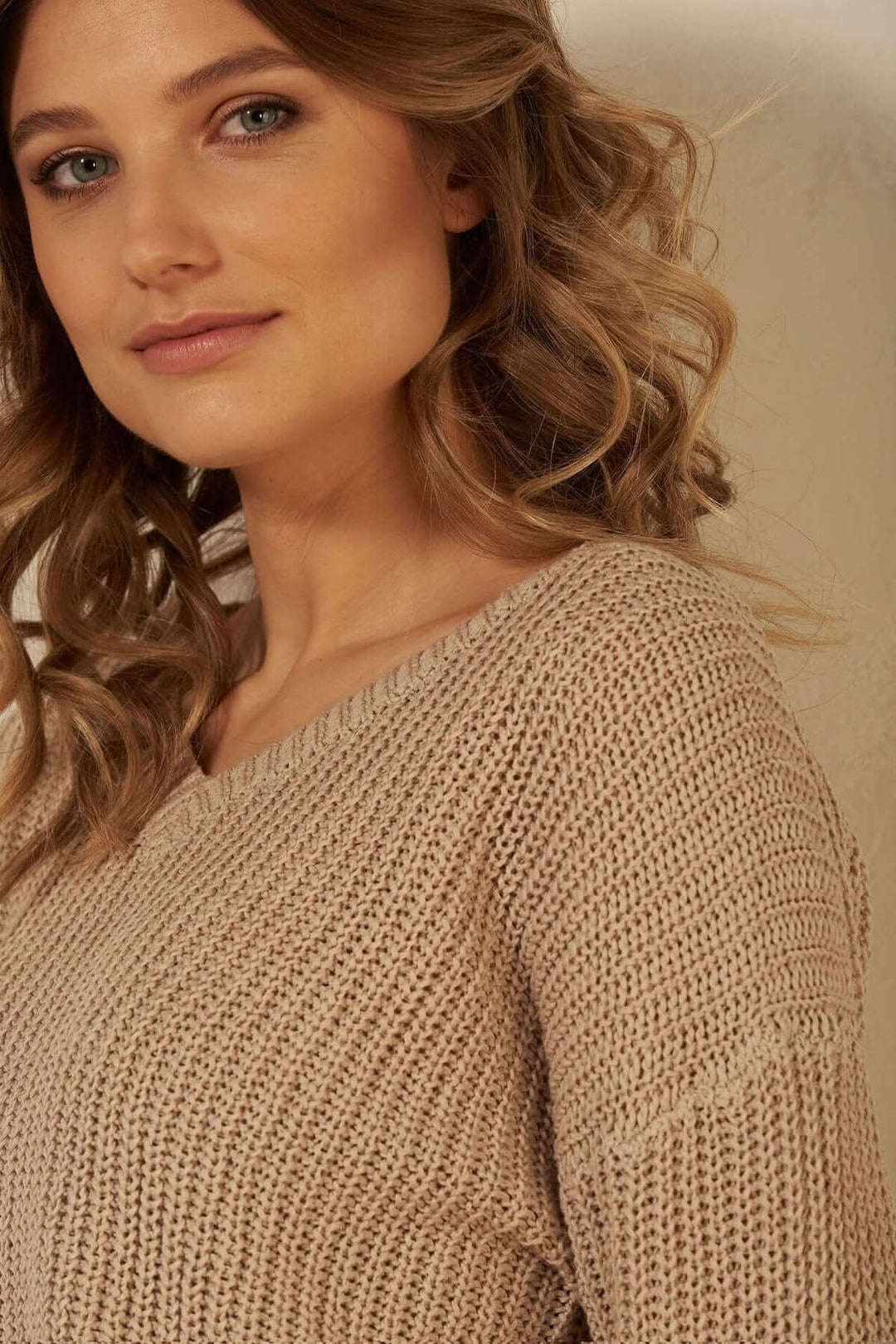 Pull à mailles en coton beige avec col en V et couture légèrement tombante.