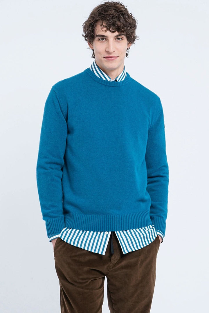 Pull en laine Shetland bleu, avec col rond, porté sur une chemise à rayures, modèle homme.