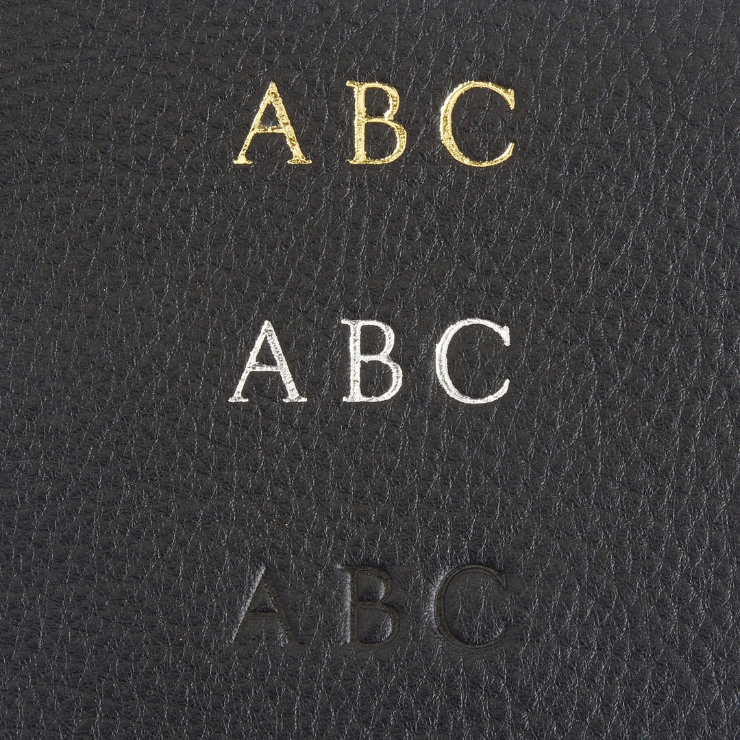 Close-up of monogrammed letters ABC in gold, silver, and black on a leather surface.