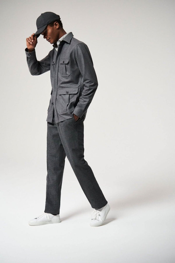 Homme en surchemise en laine cachemire, pantalon gris, et casquette, pose dynamique sur fond clair.