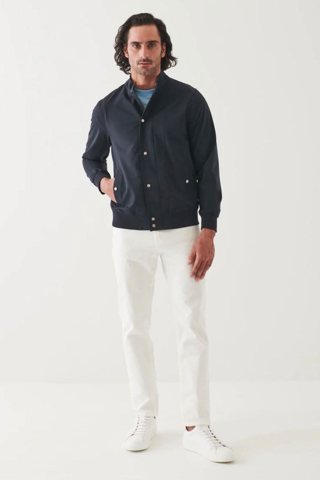 Homme portant une veste bomber en nylon navy avec un pantalon blanc et des sneakers blanches, style moderne.